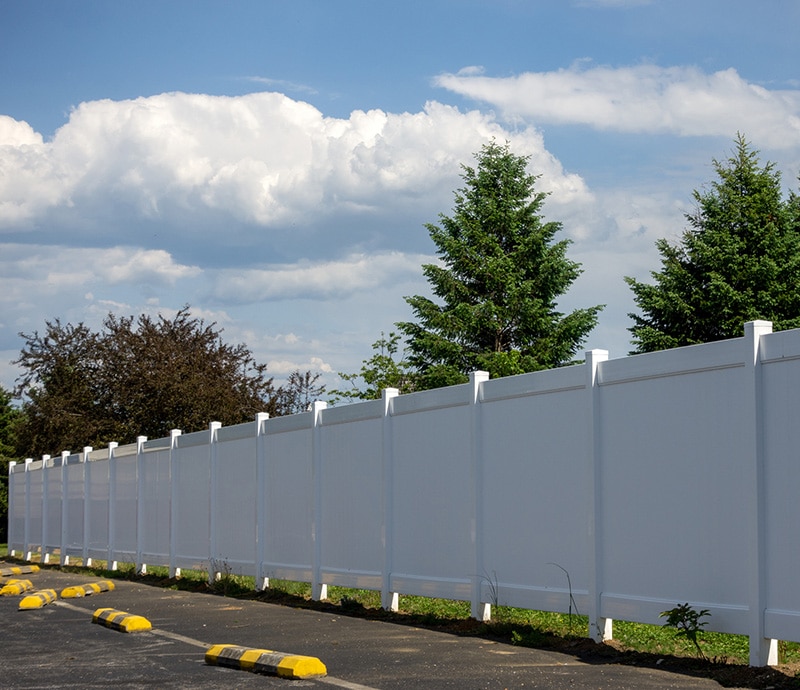 White vinyl fence installed on the perimeter of a parking lot
